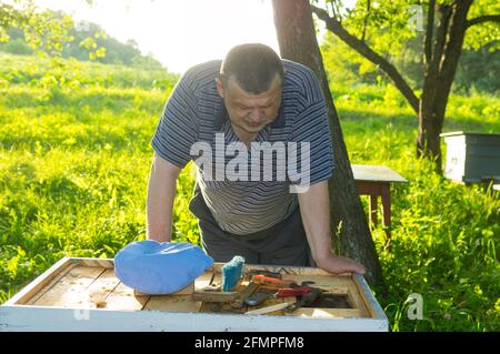 Ritratto all'aperto dell'apicoltore caucasico anziano stooped giù all'alveare un apiario e pensare Foto Stock