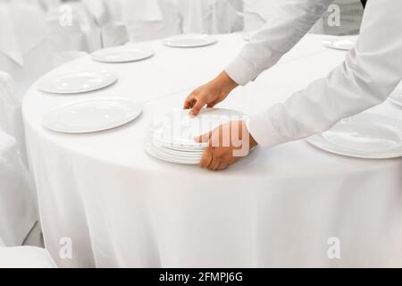 Primo piano cameriere uomo mani che serve banchetto bianco al ristorante. Foto Stock