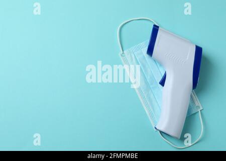 Termometro a pistola e maschera medica su sfondo blu Foto Stock