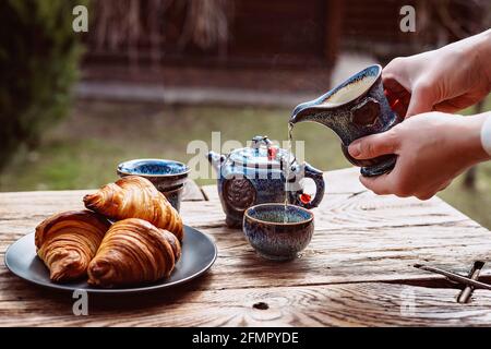 Prima colazione con tè cinese e dolci freschi, croissant al burro aromatico. Le mani delle donne versano il tè. Cerimonia del tè. Foto Stock