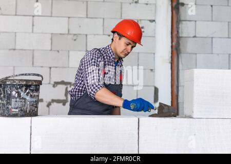 Il costruttore dell'uomo giovane mette sul blocco aerato di calcestruzzo di grout Foto Stock