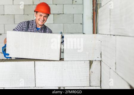 muratore a muratore che lavora con blocchi di calcestruzzo cellulare autoclavati. Walling, installazione di mattoni in cantiere, ingegneria e costruzioni con Foto Stock