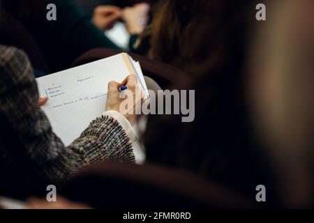 Vista posteriore di una donna che prende appunti durante una presentazione Foto Stock