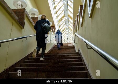 Da sotto pedoni anonimi in outerwear che salono la scalinata sotto soffitto di vetro durante il giorno Foto Stock