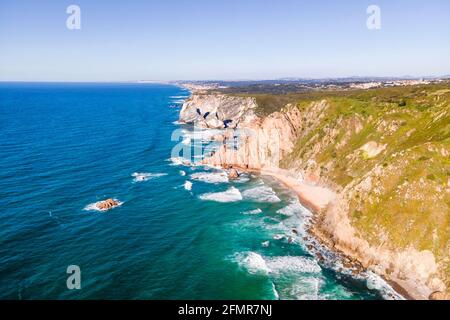 Vista aerea della costa selvaggia con scogliere e promontorio roccioso vicino a Cabo da Roca di fronte all'Oceano Atlantico, Colares, Lisbona, Portogallo. Foto Stock