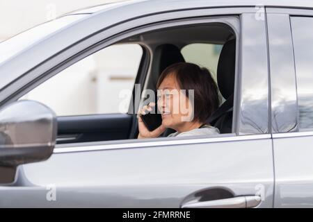 Donna asiatica matura in un'auto che parla al suo telefono Foto Stock