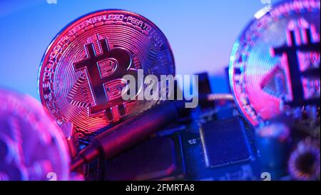 Monete in criptovaluta sulla scheda a circuito stampato. Bitcoins sulla scheda CPU. Primo piano Bitcoin con luce al neon blu e rosa. Scheda a circuito stampato con moneta Foto Stock