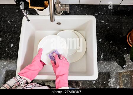 Piatti lavanti femmina corti con spugna viola sopra lavello della cucina , casalinga irriconoscibile a casa facendo i chores della famiglia, indossando gomma Foto Stock