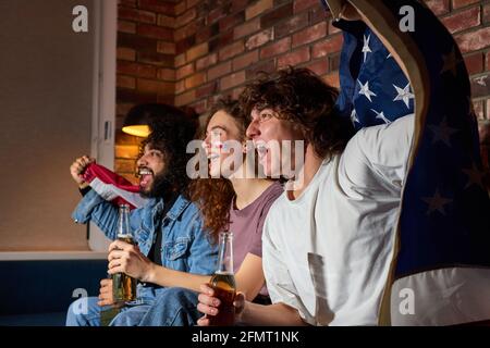 Gli appassionati di sport si aggiudicano la vittoria a casa propria. Tifosi appassionati gridano guardando la partita in TV, salutando insieme, gridando emotivamente Foto Stock