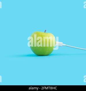Caricabatteria bianco per telefono collegato a una mela verde isolata su uno sfondo blu Foto Stock