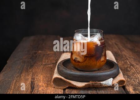 Caffè ghiacciato con latte, bevanda fredda in un bicchiere su fondo scuro. Versare il latte nel caffè. Spazio di copia. Foto Stock