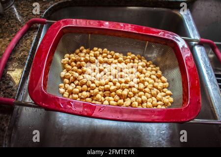 Cotti i ceci in un cestello di raccolta su un acciaio inossidabile lavello - primo piano e messa a fuoco superficiale Foto Stock