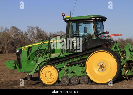 Un trattore cingolato John Deere in un campo agricolo con cielo blu e alberi nel paese. Foto Stock