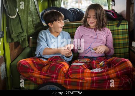 Il fratello e la sorella giocano le carte sul retro del camper VW furgone durante il viaggio Foto Stock
