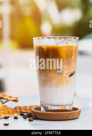 Caffè latte ghiacciato rinfrescante in un bicchiere con waffle a cuore e chicchi di caffè Foto Stock