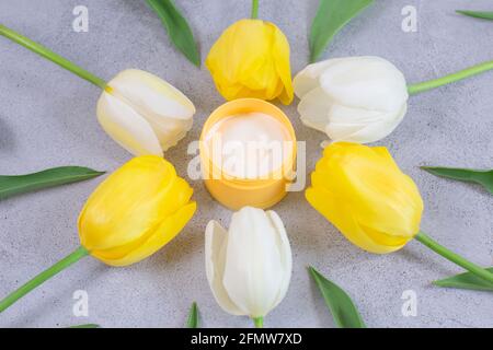 Spa concept crema in un vaso di vetro per crema intorno tulipani fiori su sfondo grigio. Spazio copia. Foto Stock