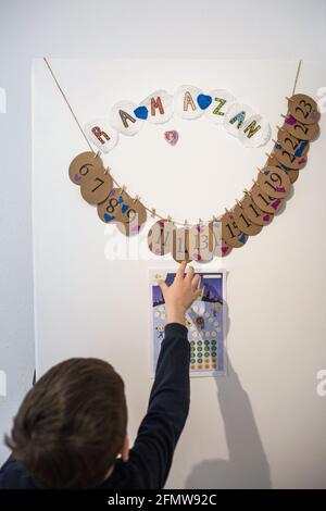 PRODUZIONE - 10 maggio 2021, Nord Reno-Westfalia, Minden: Il bambino guarda un calendario Ramadan, sul retro del quale i suoi genitori hanno scritto compiti per i bambini. Ogni giorno i bambini guardano al loro compito e ottengono una ricompensa se lo completano. Durante il giorno, i credenti in Ramadan non mangiano nulla; solo dopo il tramonto mangiano e bevono alla rottura del digiuno - iftar - e di solito in un incontro sociale. Le famiglie turche stanno cucinando e cucinando piatti tradizionali dall'inizio della settimana. Alla fine del mese di digiuno, molti devoti musulmani in Germania stanno preparando anche f Foto Stock