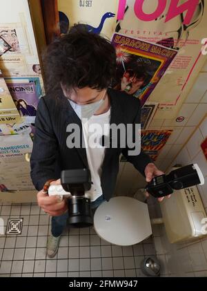 05 maggio 2021, Amburgo: Fotografo Stefan Schoder del progetto Corona Aid "Art for the loo" fotografie adesivi sulla parete della toilette del bar Kleinraumdisko a St. Pauli. Con le foto degli slogan della toilette e dei graffiti della toletta, i tre Hamburgers hanno già fornito sostegno finanziario a varie sedi di Amburgo da dicembre. Nel loro negozio online, offrono stampe di alta qualità con foto da luoghi come Elbschlosskeller, Roschinsky's e Café May. In consultazione con i bar e i club, il trio prendere le foto stessi nei bagni, modificare e infine mettere su Foto Stock
