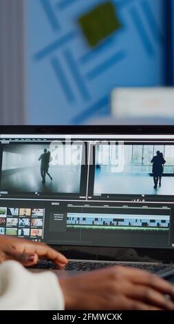 Videografo africano che lavora su un computer portatile dall'ufficio aziendale, editing di filmati e audio di notte. Creazione di contenuti utilizzando dispositivi professionali moderna tecnologia di elaborazione wireless montaggio film. Foto Stock