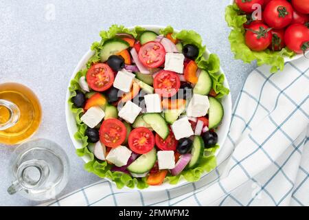 Insalata greca con pomodori ciliegini, cetrioli, formaggio feta, olive e condita con olio. Tovagliolo a scacchi bianco su un tavolo grigio. Vista dall'alto. Piatto com Foto Stock