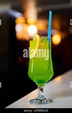 Cocktail alcolico verde con arancia, ghiaccio e paglia. Primo piano, messa a fuoco selettiva Foto Stock