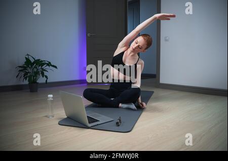 Durante l'auto-isolamento, la ragazza prende una lezione di yoga a casa, esegue esercizi di stretching. Foto Stock