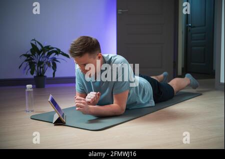 Dopo un duro allenamento domestico con l'aiuto di Internet e di un tablet, l'atleta in uniforme sportiva è stanco. Foto Stock