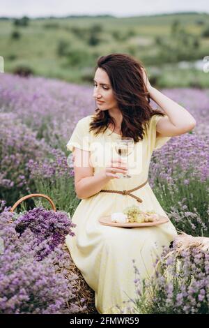 Giovane bella donna in abito con un bicchiere di vino in un campo di lavanda. Messa a fuoco selettiva morbida, rumore ART Foto Stock