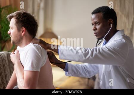 Medico africano che esamina i polmoni e il cuore dei giovani pazienti maschi che ascoltano Foto Stock