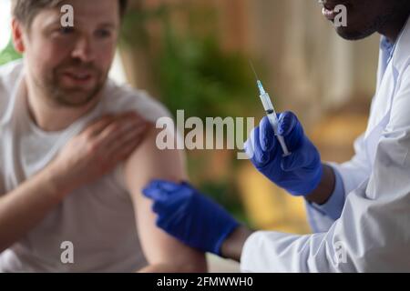 Medico africano con siringa che fa l'iniezione di vaccino a maschio paziente Foto Stock