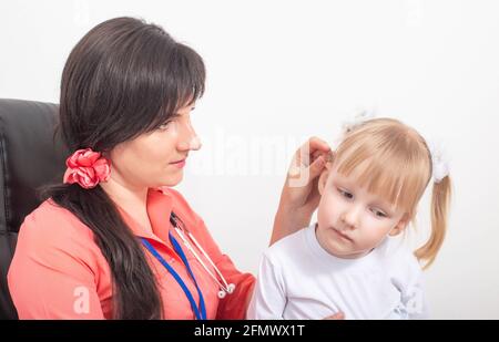 Dottore otolaringologo pediatrico esamina l'orecchio di un bambino di una bambina il cui tappo sulfureo nell'orecchio, sfondo, intasamento Foto Stock