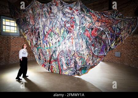 Il responsabile delle operazioni e delle strutture Sarah Morton esamina una nuova importante commissione di arazzi su larga scala dell'artista Christian Newby dal titolo "Flower-Necklace-Cargo-Net" in esposizione nello spazio espositivo del City Dome presso Collective on Calton Hill, Edimburgo. La nuova mostra si apre al pubblico giovedì 13 maggio e segna l'inizio del programma artistico di CollectiveÕs 2021 a seguito del recente periodo di chiusura a causa del blocco. Data immagine: Mercoledì 12 maggio 2021. Foto Stock