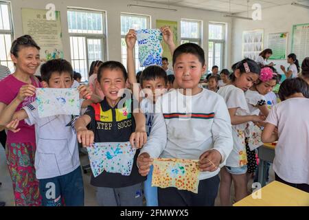 Studenti di una scuola elementare nella Cina rurale che lavorano su un progetto artistico e artigianale. Foto Stock