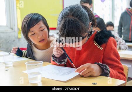 Gli studenti primari che si godono la loro pittura con acqua in una scuola rurale in Cina. Foto Stock