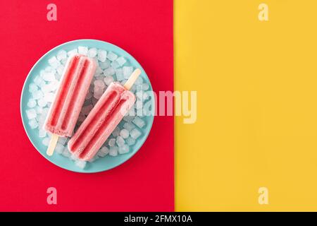 Popsicle di fragole con ghiaccio su sfondo giallo e rosso Foto Stock