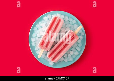 Popsicle di fragole con ghiaccio su sfondo rosso Foto Stock