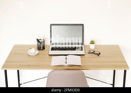 Computer portatile, appunti, pianta casa cactus, forniture e vetri ripiegati su scrivania in legno, sedia grigia in ufficio pieno di luce solare. Designer creativi w Foto Stock