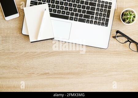 Composizione minimalistica a disposizione piatta con tastiera per computer portatile in bianco e nero, gadget per telefoni cellulari, tazza di caffè e bicchieri ripiegati su scrivania in legno testurizzato Foto Stock