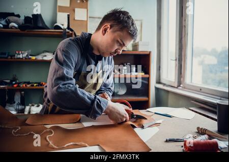Un giovane ragazzo di talento aiuta suo padre nel commercio di famiglia, taglia fuori gli sbozzi per le scarpe dalla pelle. Foto Stock