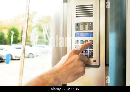 Primo piano della mano dell'uomo che immette il codice del sistema di sicurezza, premendo il tasto con il dito indice sul moderno dispositivo intercom con schermo lcd blu vicino entrence doo Foto Stock