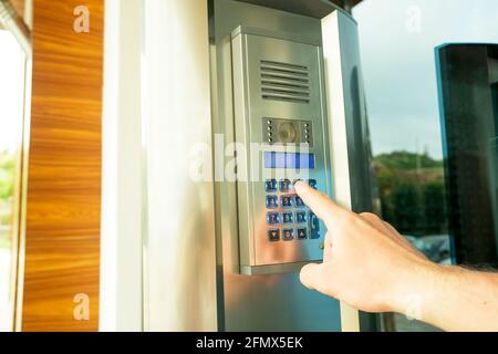 Primo piano della mano dell'uomo che immette il codice del sistema di sicurezza, premendo il tasto con il dito indice sul moderno dispositivo intercom con schermo lcd blu vicino entrence doo Foto Stock