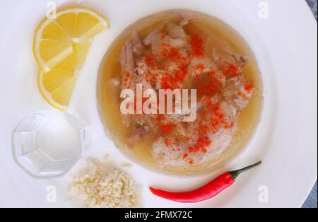 Maiale ungherese in gelatina, kocsonya, con peperoncino rosso, limone, rafano grattugiato, Paprika, accompagnata da un bicchiere di Palinka (acquavite di frutta ungherese). Foto Stock