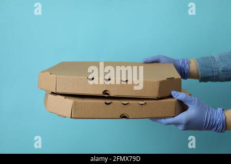 Le mani in guanti tengono le scatole della pizza su sfondo blu Foto Stock