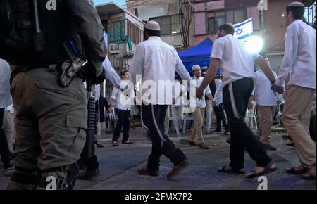 Un poliziotto di confine armato è in guardia mentre i coloni ebrei cantano e ballano di fronte a una casa che è stata occupata dai coloni ebrei a Sheikh Jarrah, un quartiere prevalentemente palestinese il 07 maggio 2021, a Gerusalemme est, Israele. Decine di residenti palestinesi dello sceicco Jarrah hanno dovuto affrontare per anni un potenziale sfratto, in mezzo a sforzi intensificati da parte di gruppi di coloni di destra che affermano che la terra era di proprietà degli ebrei prima del 1948, quando fu fondato Israele. La minaccia dello sfratto ha portato a frequenti proteste. Foto Stock