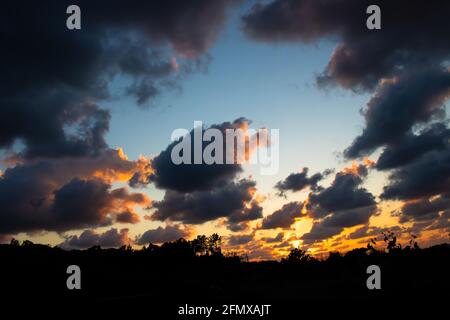 Tramonto spettacolare con nuvole scure e pesanti che incorniciano il blu e. cielo arancione sopra la silhouette di campagna campo agricolo Foto Stock