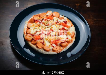 Pizza, salsiccia e bastoncini di granchio in un piatto di ceramica su un tavolo di legno. Foto Stock