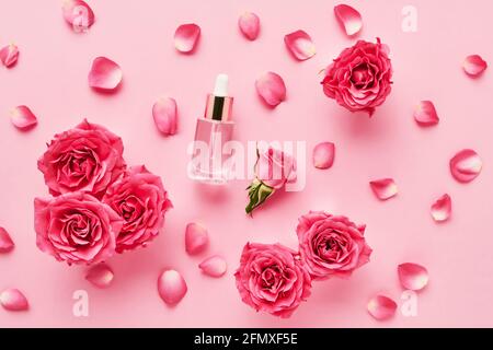 Flacone contagocce in vetro trasparente per uso medico e cosmetico e rose rosa su fondo rosa. Concetto DI SPA. Vista dall'alto, spazio di copia per il testo Foto Stock