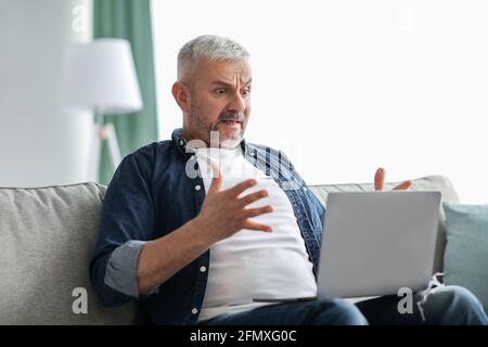 Uomo anziano sconvolto che guarda lo schermo del notebook Foto Stock