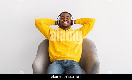 Afroamericano Guy ascolto di musica indossando cuffie, sfondo grigio Foto Stock