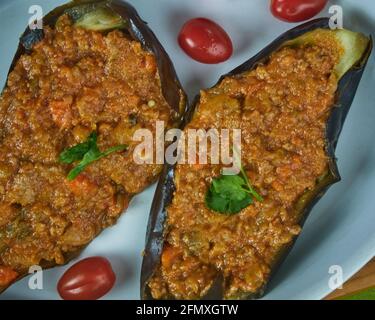 Melanzane ripiene, melanzane con salsa bolognese e pomodori ciliegini freschi in un piatto di ceramc. Vista in alto e in primo piano Foto Stock